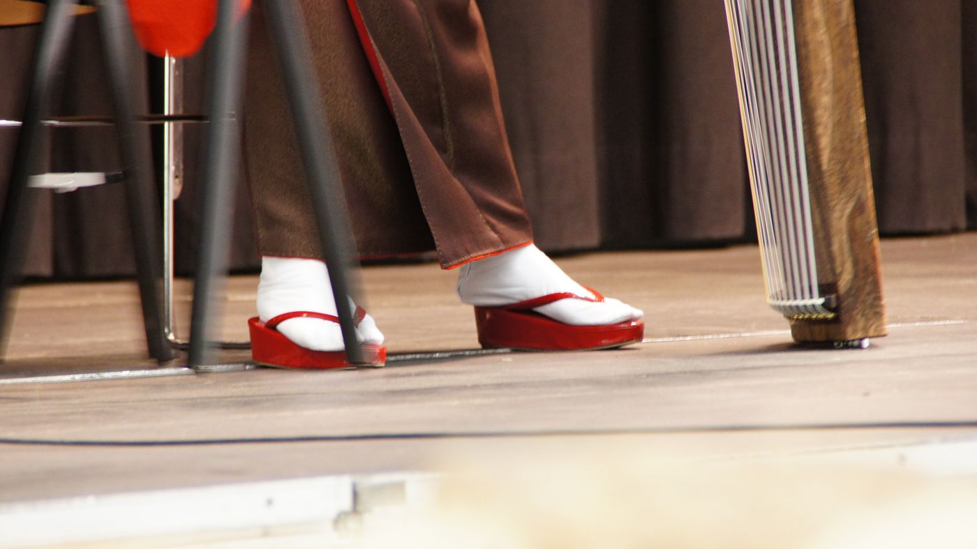 Füße in Tabi-Socken und roten Holzsandalen auf der Bühne